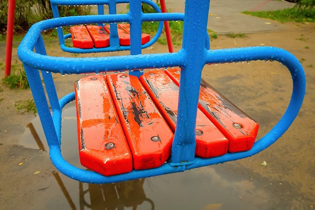 A wet playground swing hangs over a mud puddle after severe weather