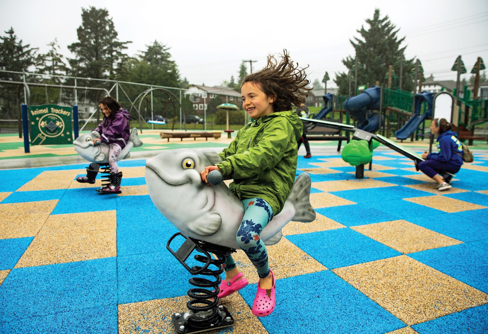 A child plays on a spring rider on an interlocking rubber tiled surface.