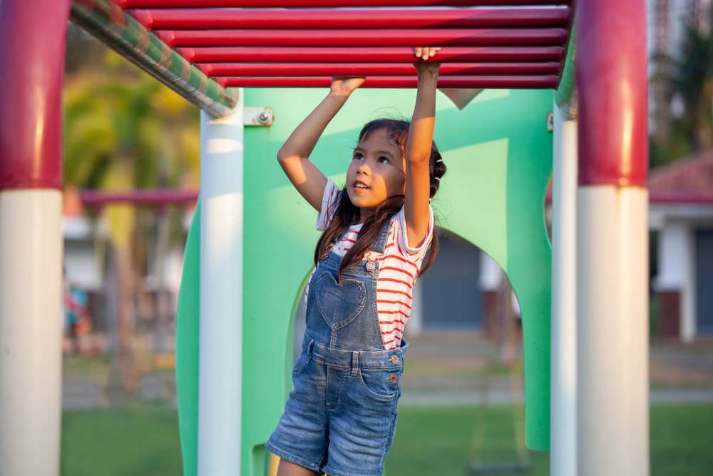 A child plays on the monkey bars over a safe playground surface.